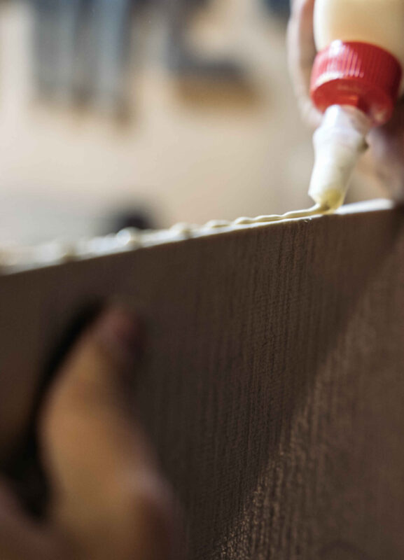 Unrecognized luthier working in his workshop and using glue in a wood board.