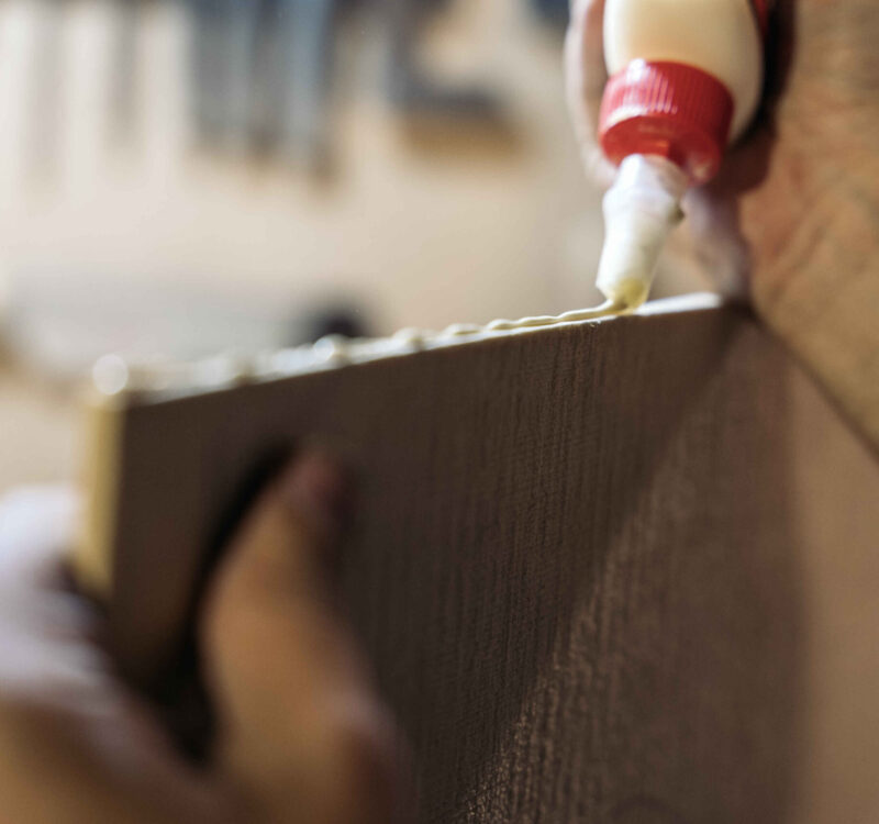 Unrecognized luthier working in his workshop and using glue in a wood board.