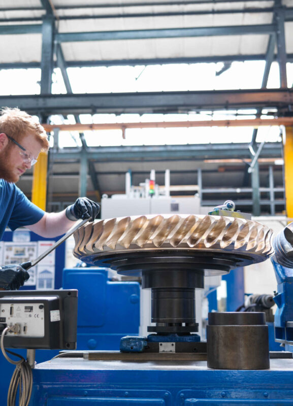 Engineer finishing bronze gear wheel in engineering factory